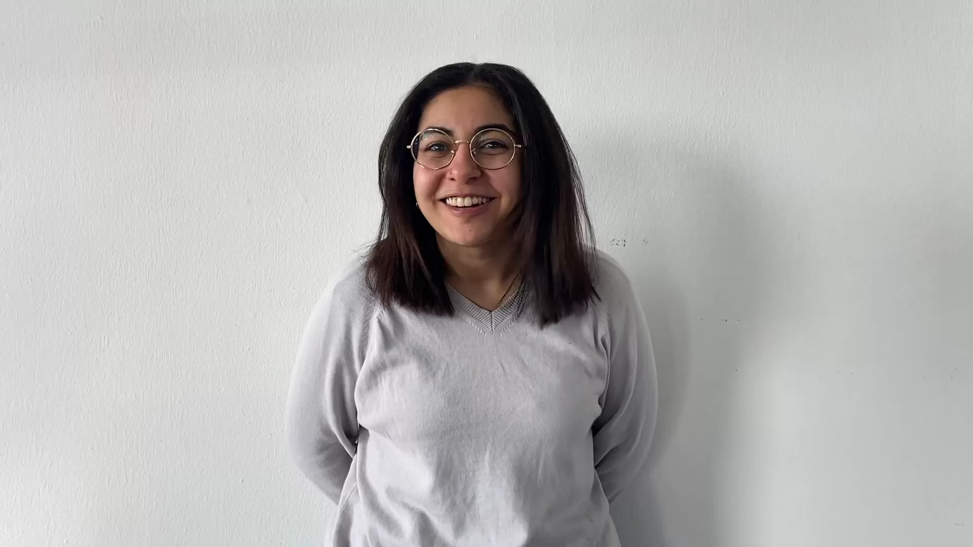 Eine junge Frau steht lächelnd vor einer weißen Wand