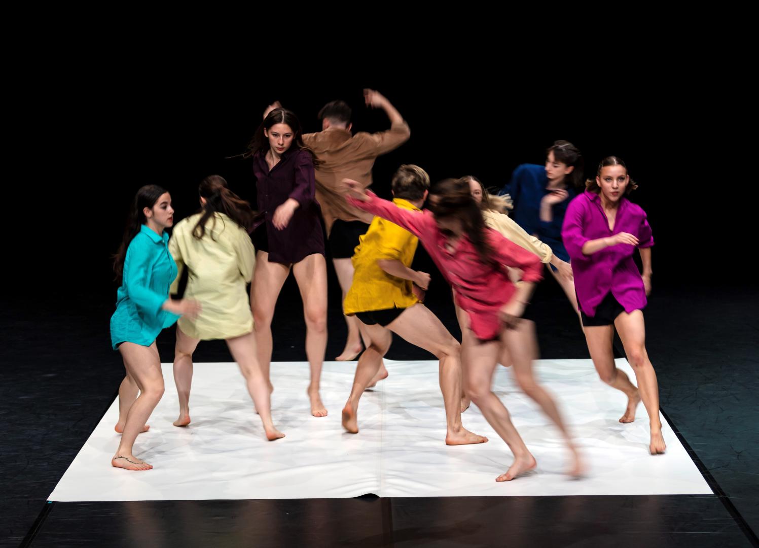 Gruppe von 8 Tänzer*innen in bunten Hemden, in dynamischer Bewegung fotografier.