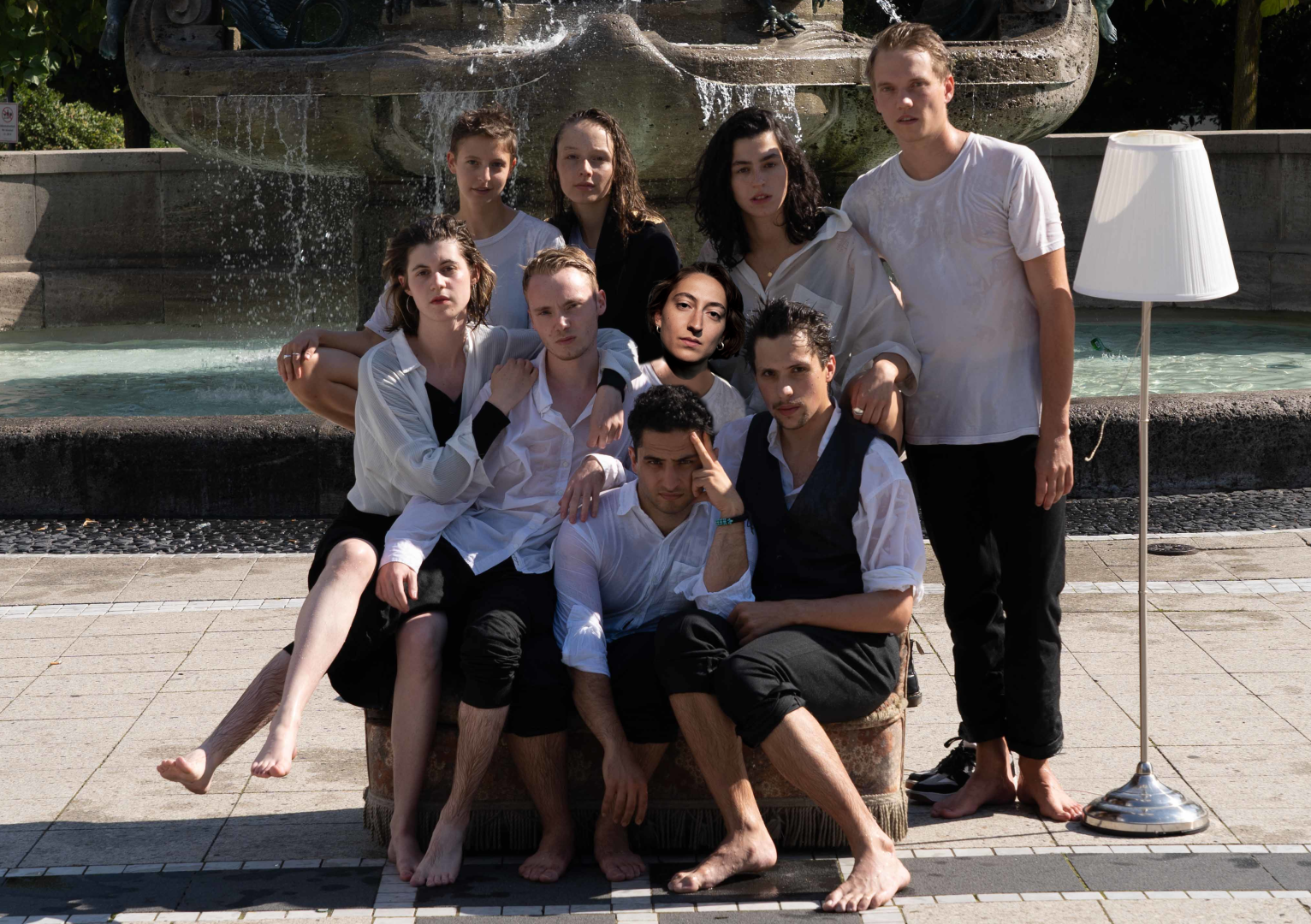Gruppenfoto mit neun Absolvierenden vor einem Brunne, alle sind nass.
