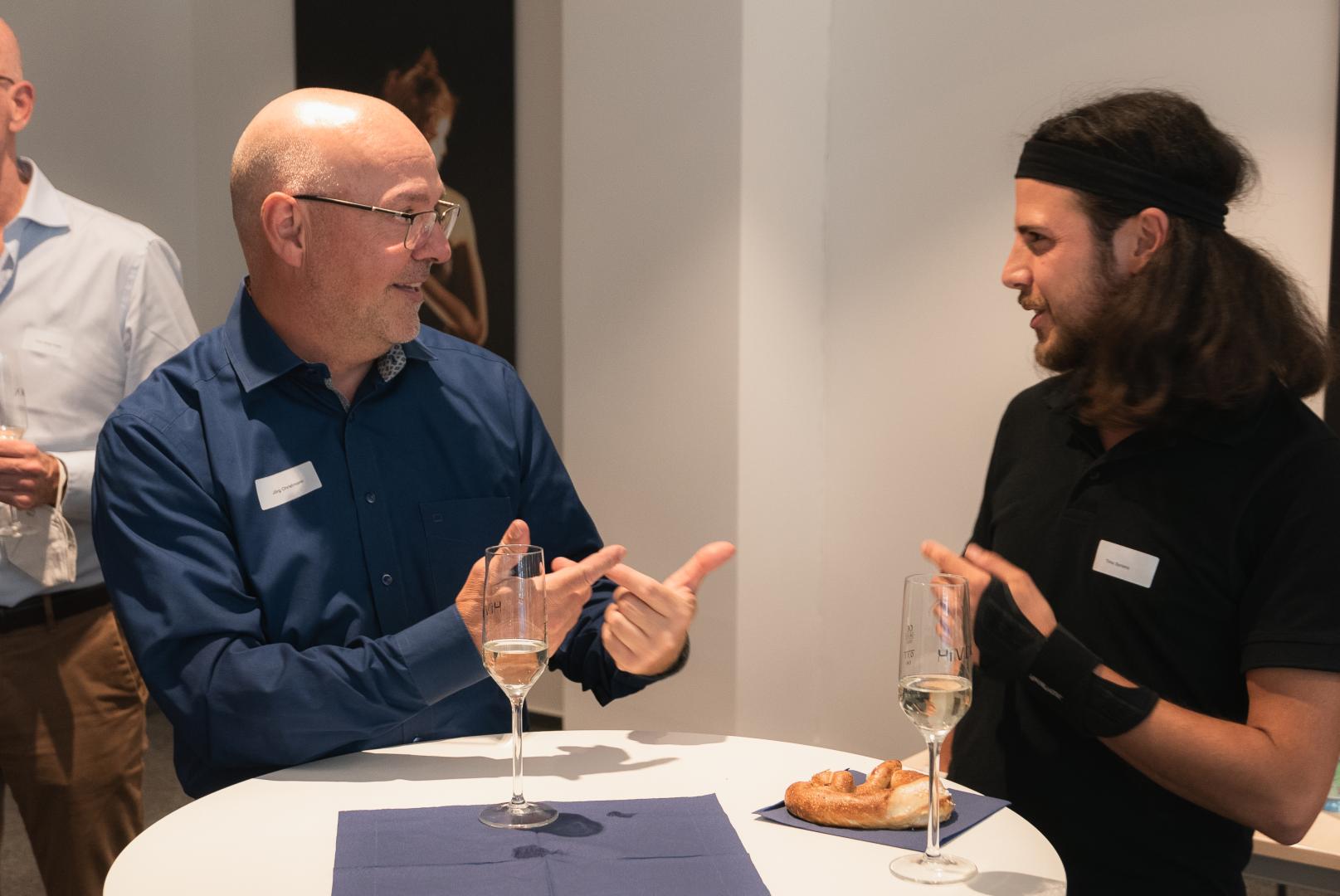 Jörg Christmann, Geschäftsführer der Carls-Stiftung, im Gespräch mit dem Studenden Timo Soriano. Vor ihnen auf einem Tisch zwei Sektgläser.