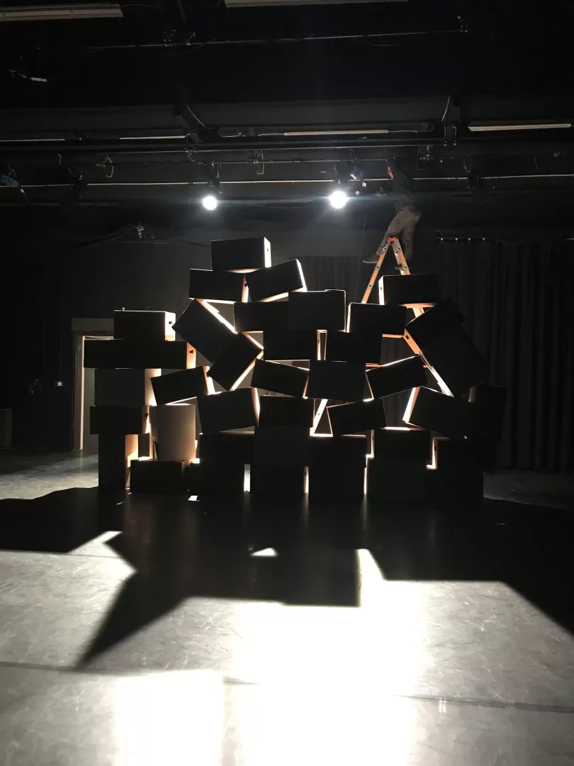 Ein schwarzer Raum, in dem Kisten aufeinandergestapelt sind, die von hinten beleuchtet werden