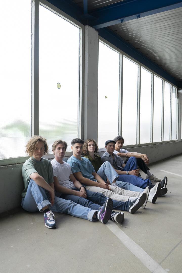 Gruppenfoto der sechs Schauspielabsolvierenden 2023. Alle auf dem Boden sitzend vor einer Fensterfront.