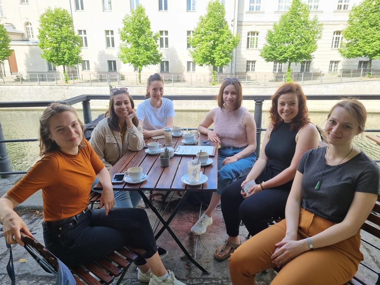 Gruppenfoto der TheO-Studierenden und der KM-Magazin Chefredakteurin an einem Cafe-Tisch draußen.