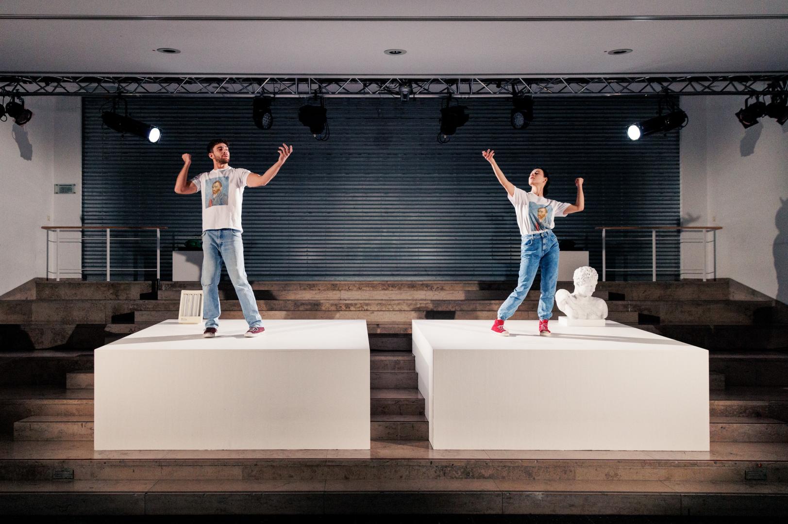 Schauspieler und Schauspielerin auf Podesten in Posen einer antiken Statue.
