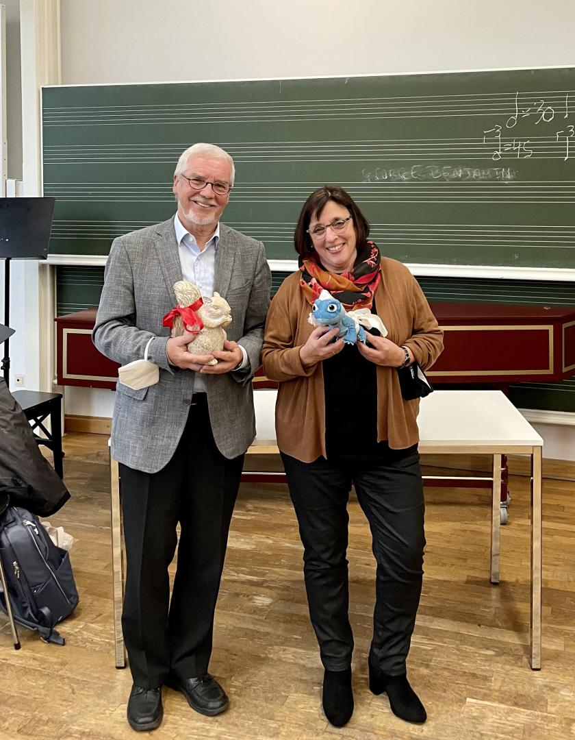Joachim Eichhorn und Bruni Böhm stehen mit einem Geschenk vor einer Tafel und lächeln in die Kamera