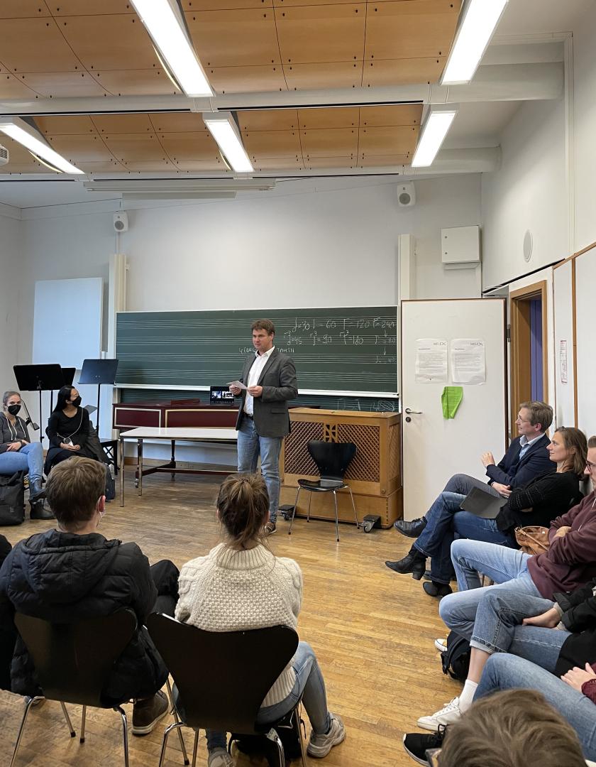 Stefan Viegelahn steht und redet, Studierende und Lehrende sitzen um ihn herum