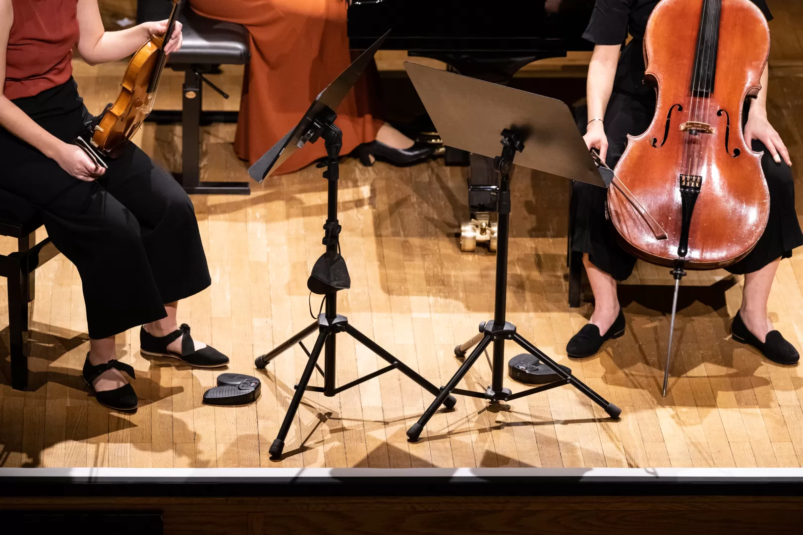 Bildausschnitt eines Kammermusik-Trios: Füße, Hände und Instrumente.