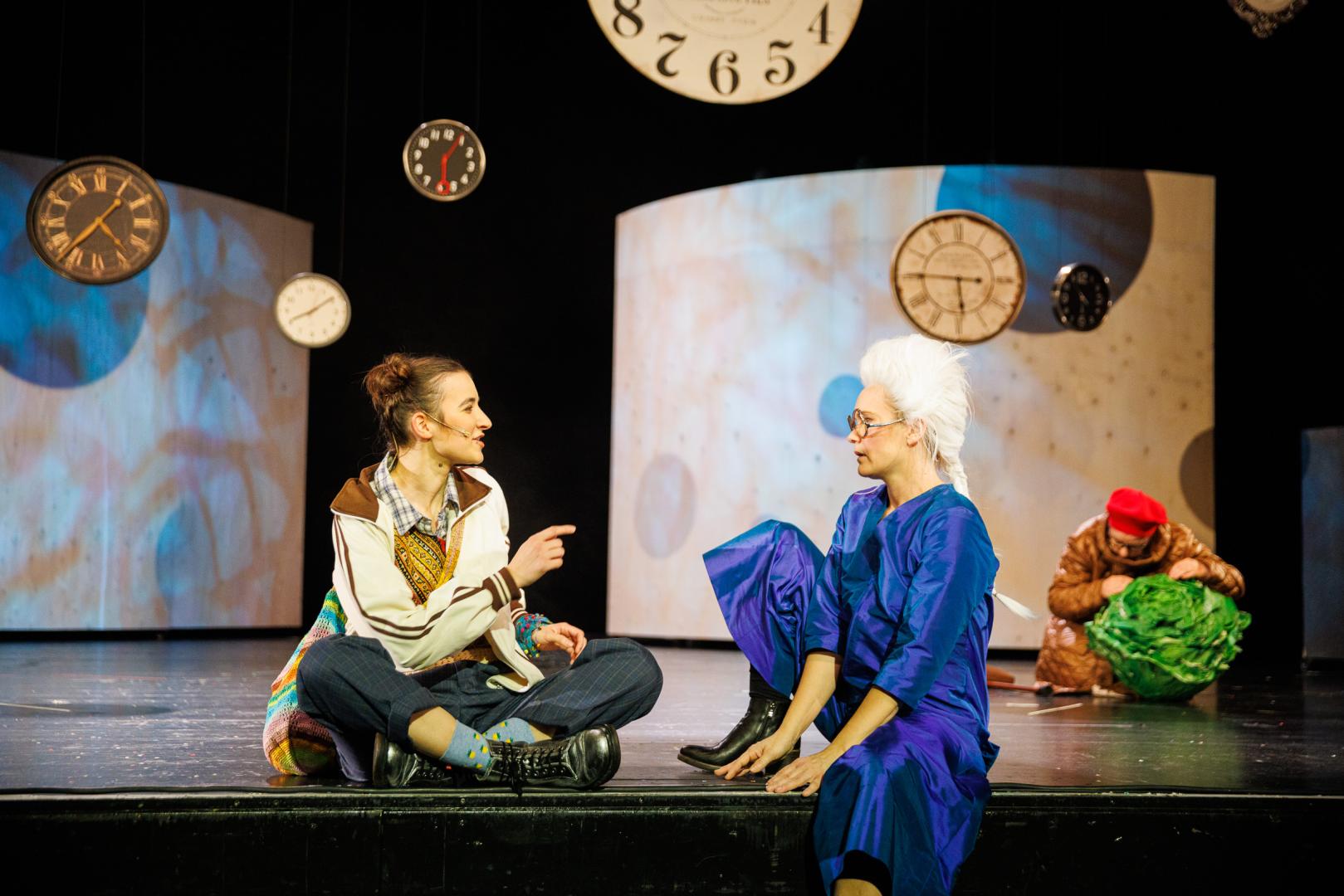 Zwei Schauspielerinnen sitzen am Bühnenrand und unterhalten sich.