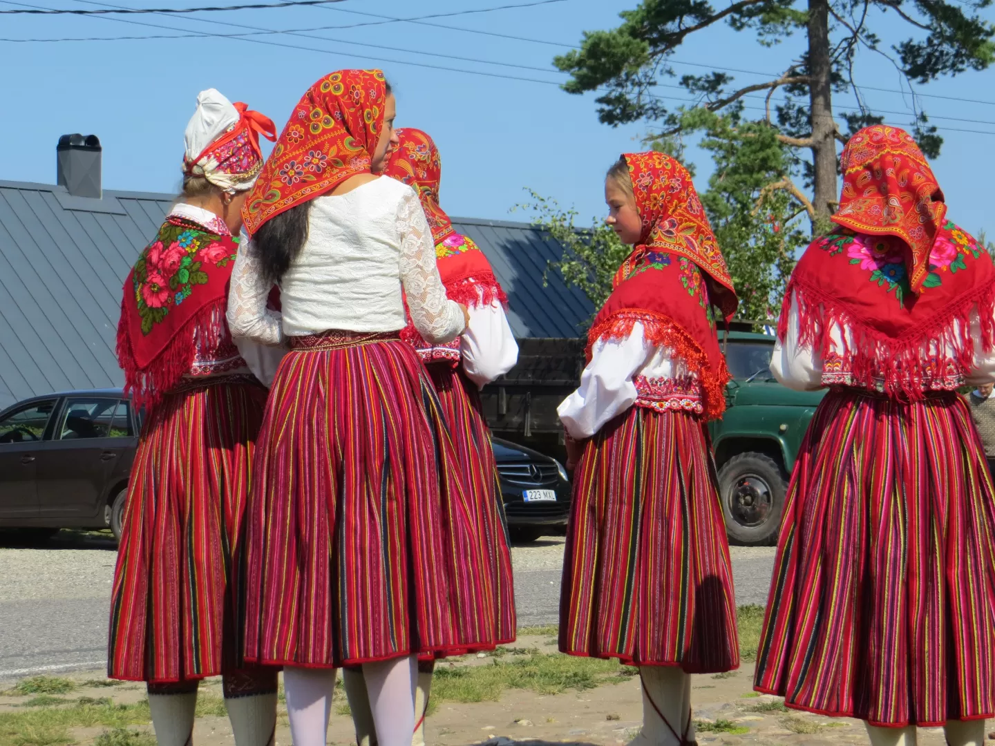 Fünf Frauen stehen im Freien beieinander, sie tragen alle eine einheitliche traditionelle Kleidung mit einem roten knielangen Rock und rotem Kopftuch.