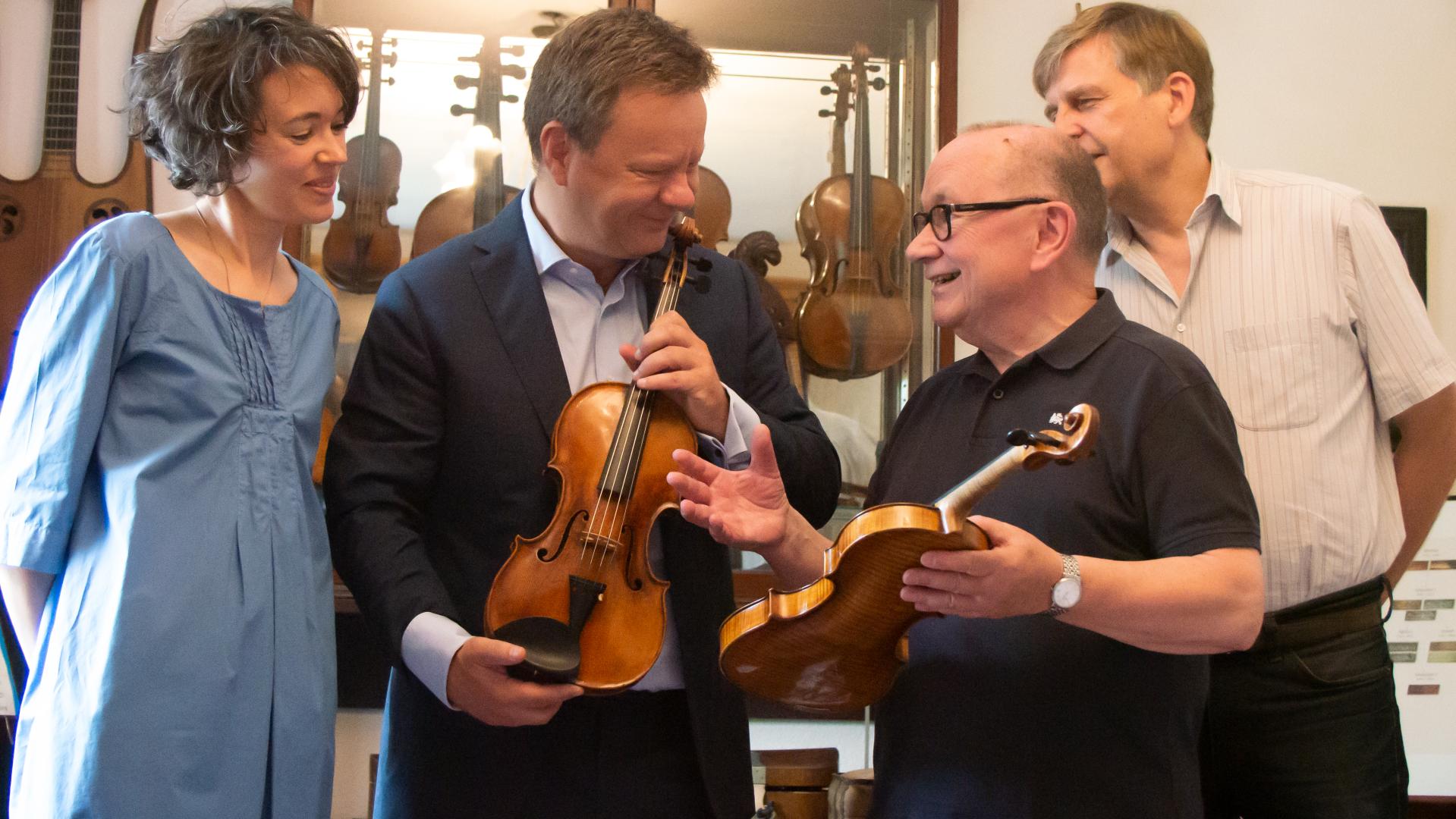 Vier Personen, in der Mitte halten Prof. Tim Vogler und Udo Schweickhardt zwei Geigen in den Händen.