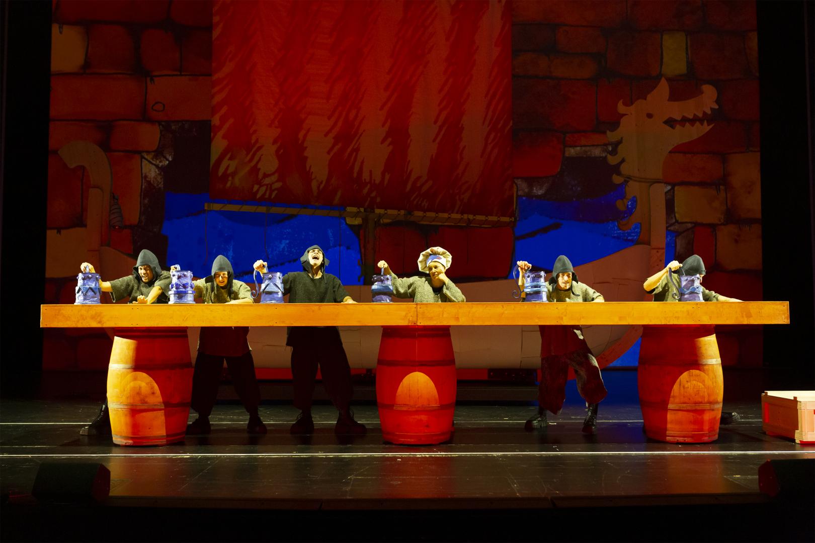 Wirtshaus, sechs Schauspielende die singend große Bierkrüge halten.