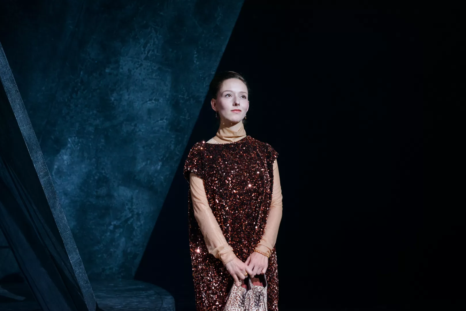 Schauspielerin in einem Paillettenkleid und mit ihren Schuhen in der Hand schaut verträumt.