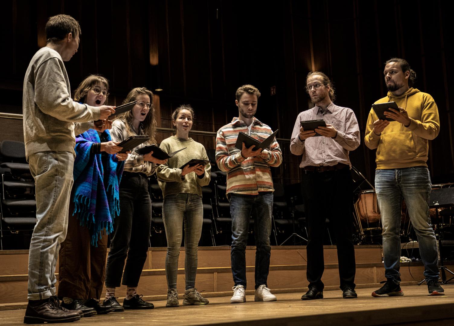 Vokalensemble mit 7 Sänger*innen auf der Bühne des Großen Saals während einer Probe.