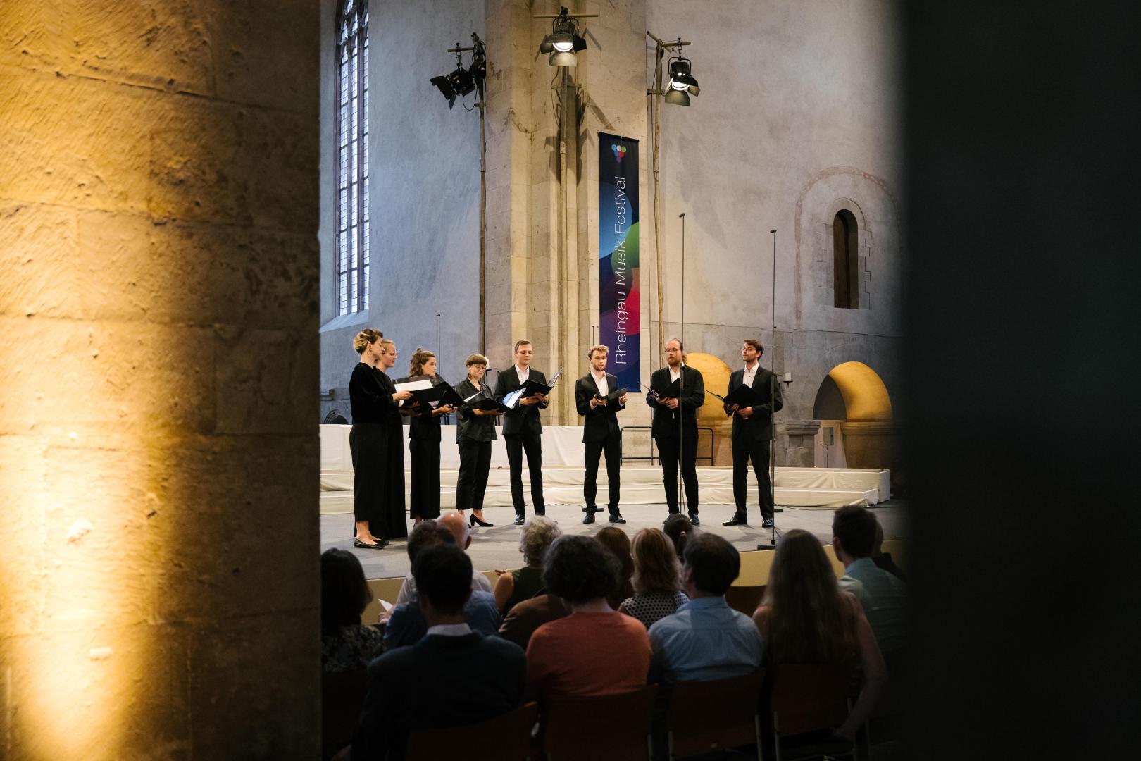 Die acht Sänger*innen des Ensembles Et Hepera auf der Bühne im Kloster Eberbach. Im Vordergrund ist Publikum zu sehen.