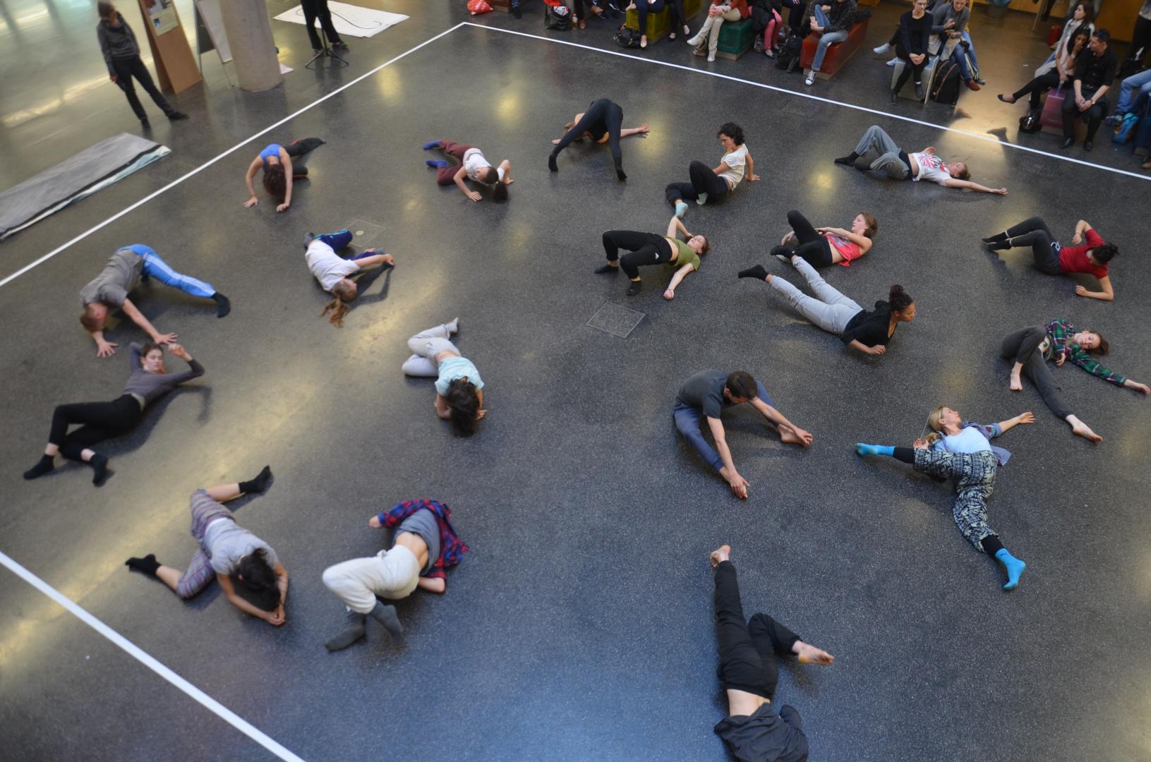 Eine große Gruppe Tänzer*innen auf dem Boden verteilt, von oben fotografiert.