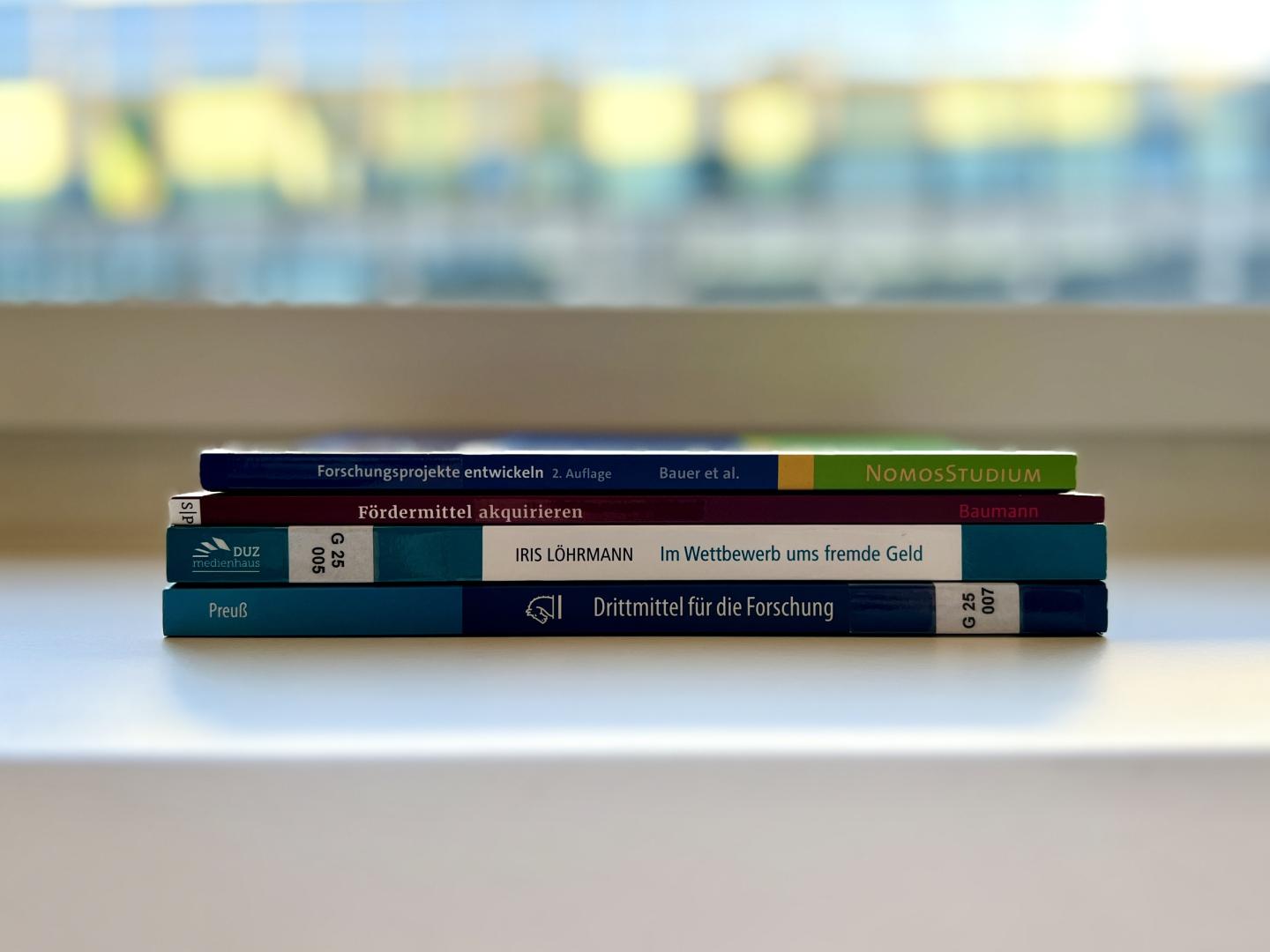 Ein Buchstapel mit den vier Büchern zum Thema Forschungsförderung, die für die Bibliothek der HfMDK angeschafft wurden.