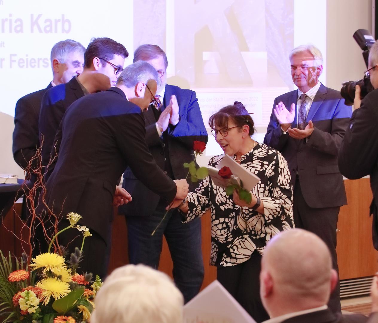 Applaudierende Menschen, eine Maria Karb in der Mitte erhält Rosen 