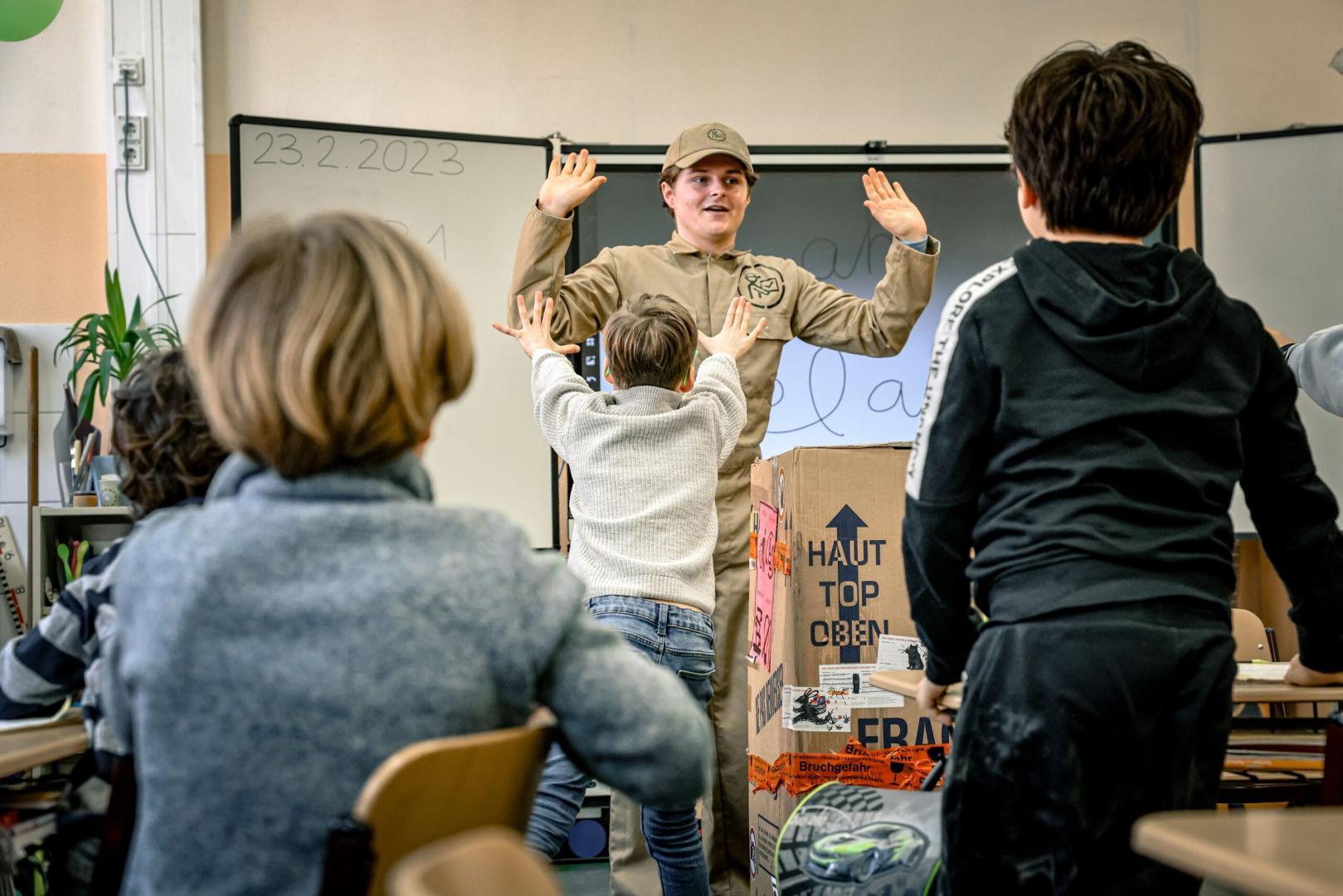 Ein Paketbote steht vor einer Schulklasse.