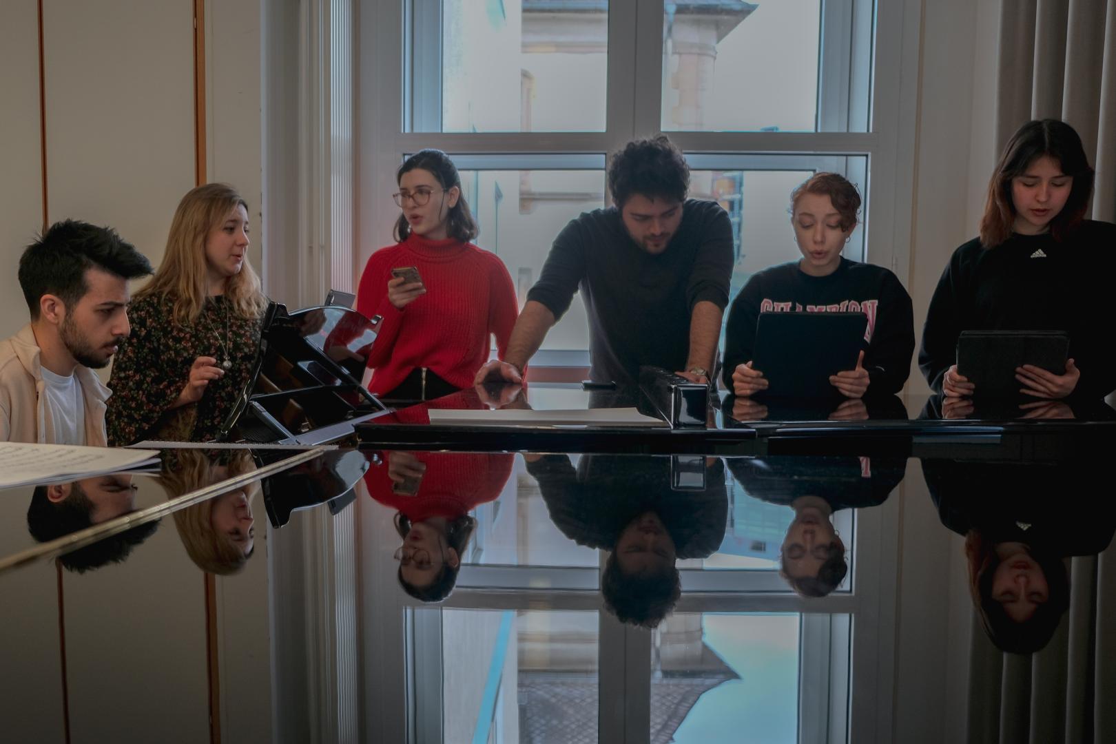 Probe, bei der 6 Musiker*innen singend um einen Flügel herum stehen.