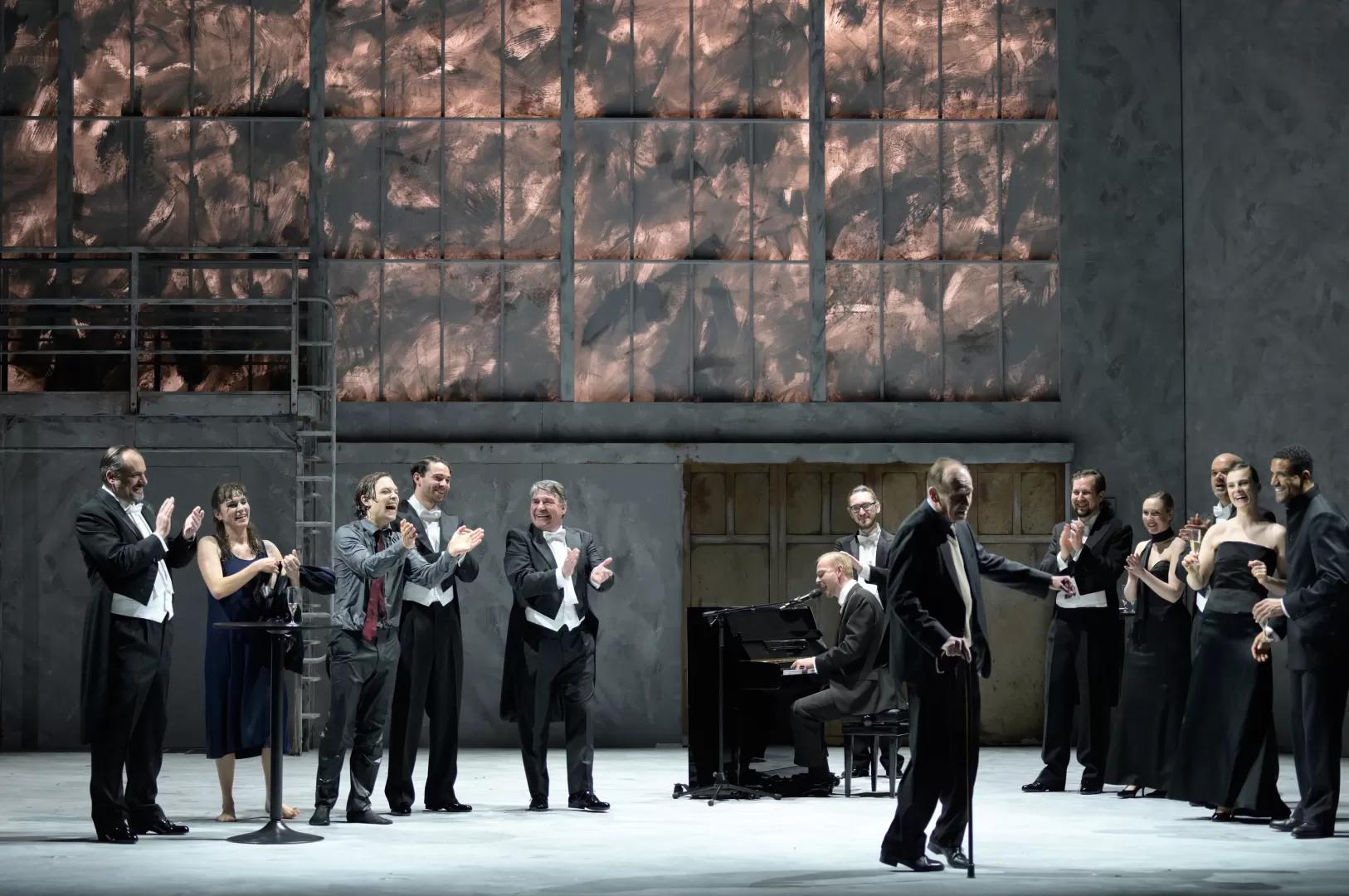 Schauspieler im Vordergrund tanzt am Gehstock, um ihn herum klatschen viele Personen.