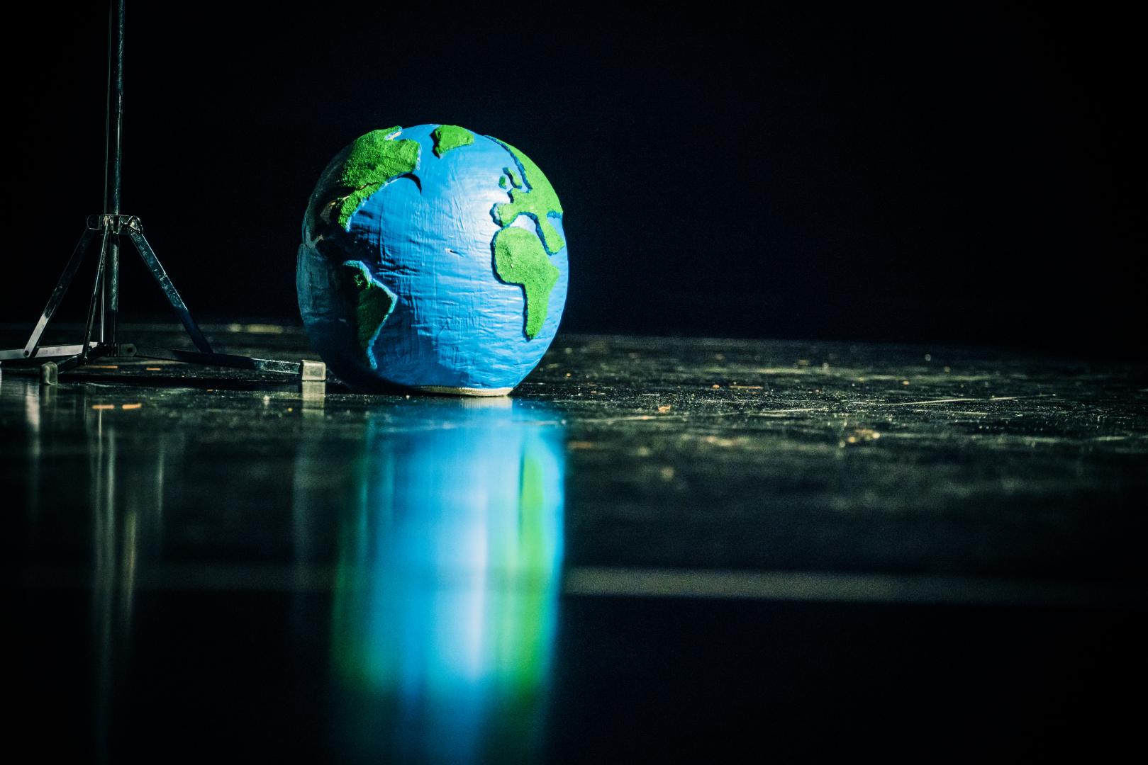 Ein Modell der Erde liegt auf dem Boden einer schwarzen Bühne.