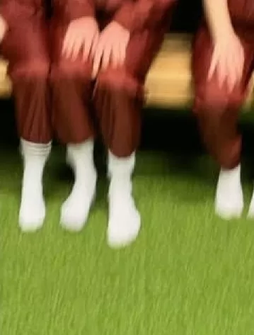 Unscharfer Blick auf drei Personen, die auf einer Holzbank sitzen und von denen nur die Beine und Füsse zu sehen sind und die rote Hosen und weisse Socken tragen.