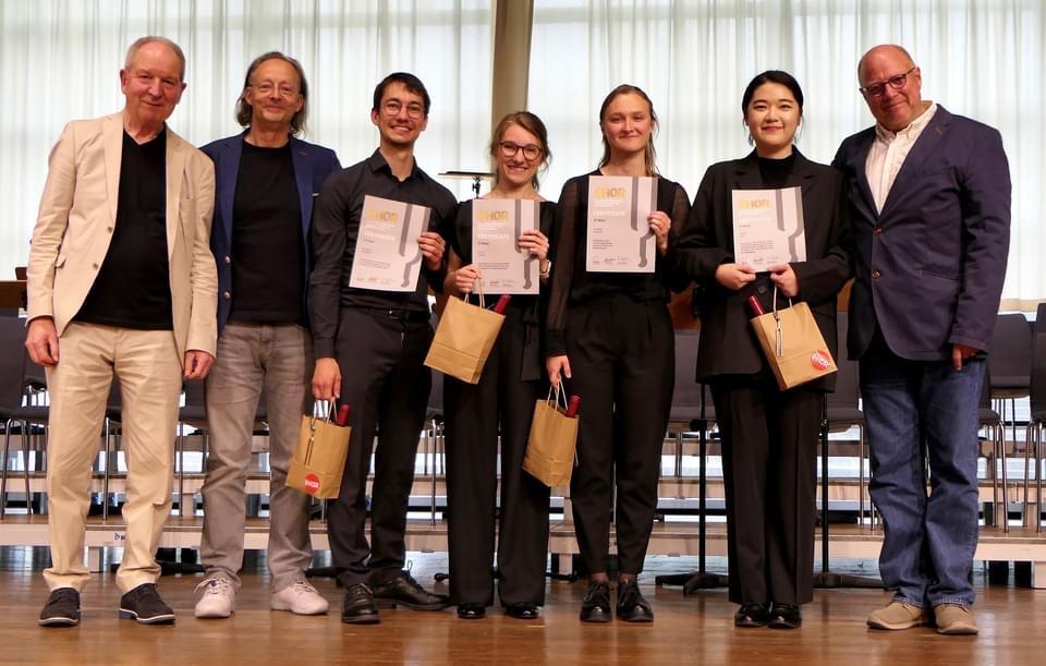 Gruppenfoto von sieben nebeneinander stehenden Personen. Vier halten Urkunden in die Kamera.