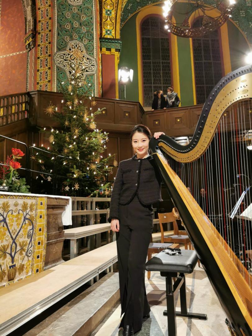 Nan Wang steht in schwarzer Konzertkleidung neben einer Harfe in einer Kirche.