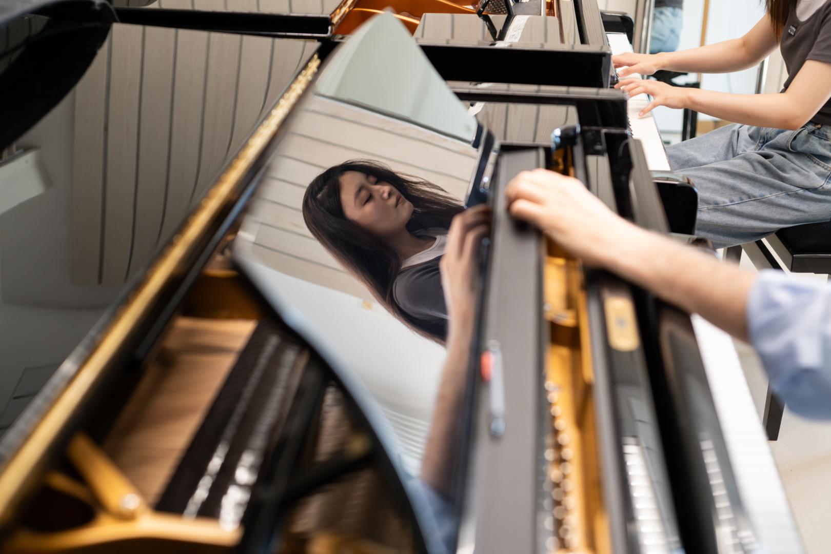 Klavier-Einzelunterricht: Das Gesicht der Studentin spiegelt sich im glänzenden Lack des Flügels.