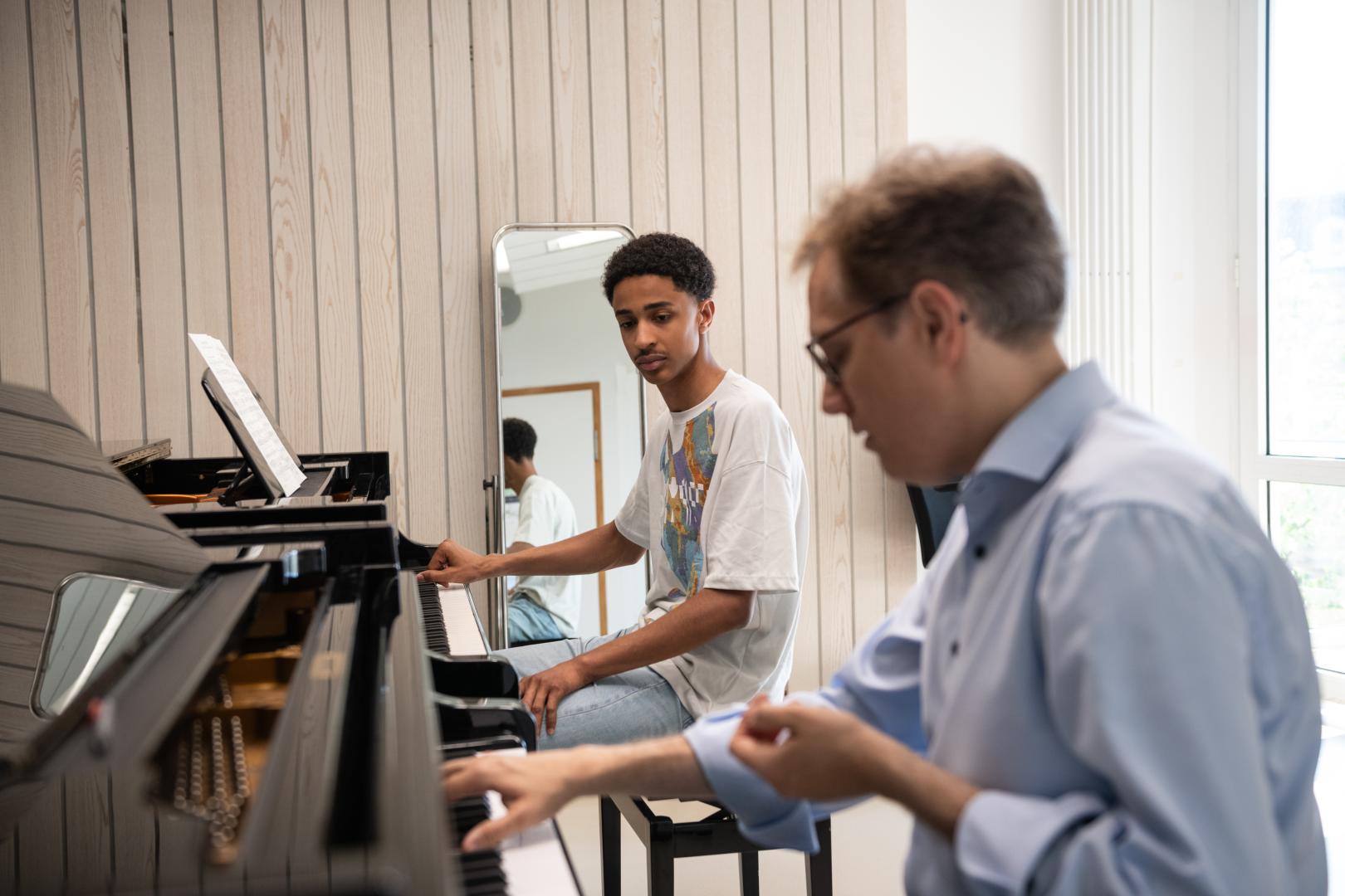 Ein Student der Young Academy im Klavier-Einzelunterricht. Er blickt auf die Hände seines Professors, der am zweiten Flügel sitzt und etwas erklärt.