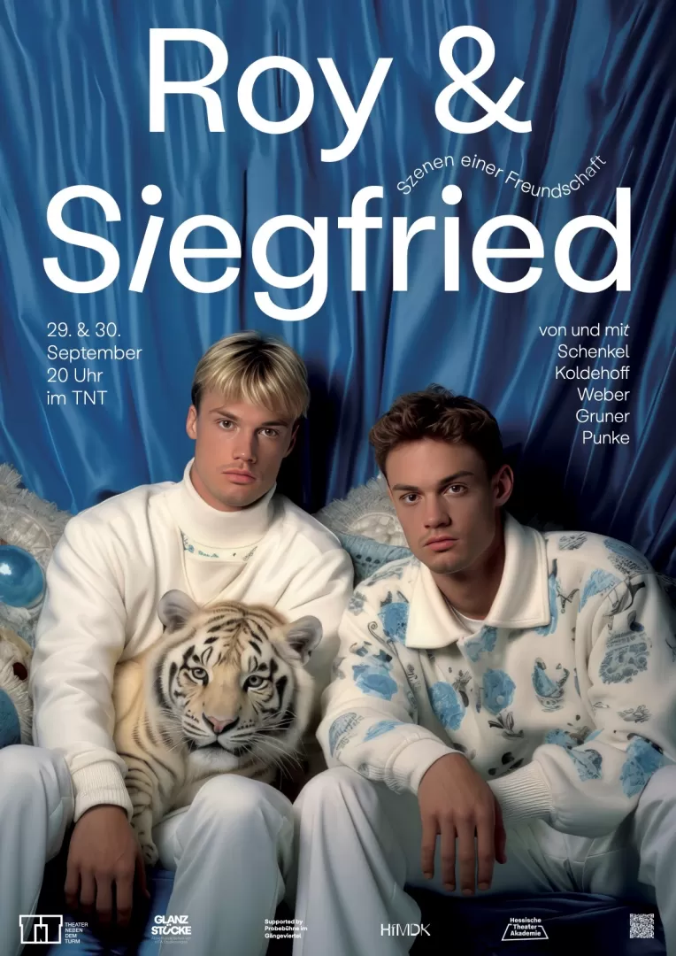 Zwei Männer sitzen nebeneinander und blicken in die Kamera. Beide sind in hellen Farbtönen, größenteils weiß bekleidet. Einer der Männer ist blond, der andere dunkelhaarig. Der linke Mann hat einen kleinen weißen Tiger auf dem Schoß.