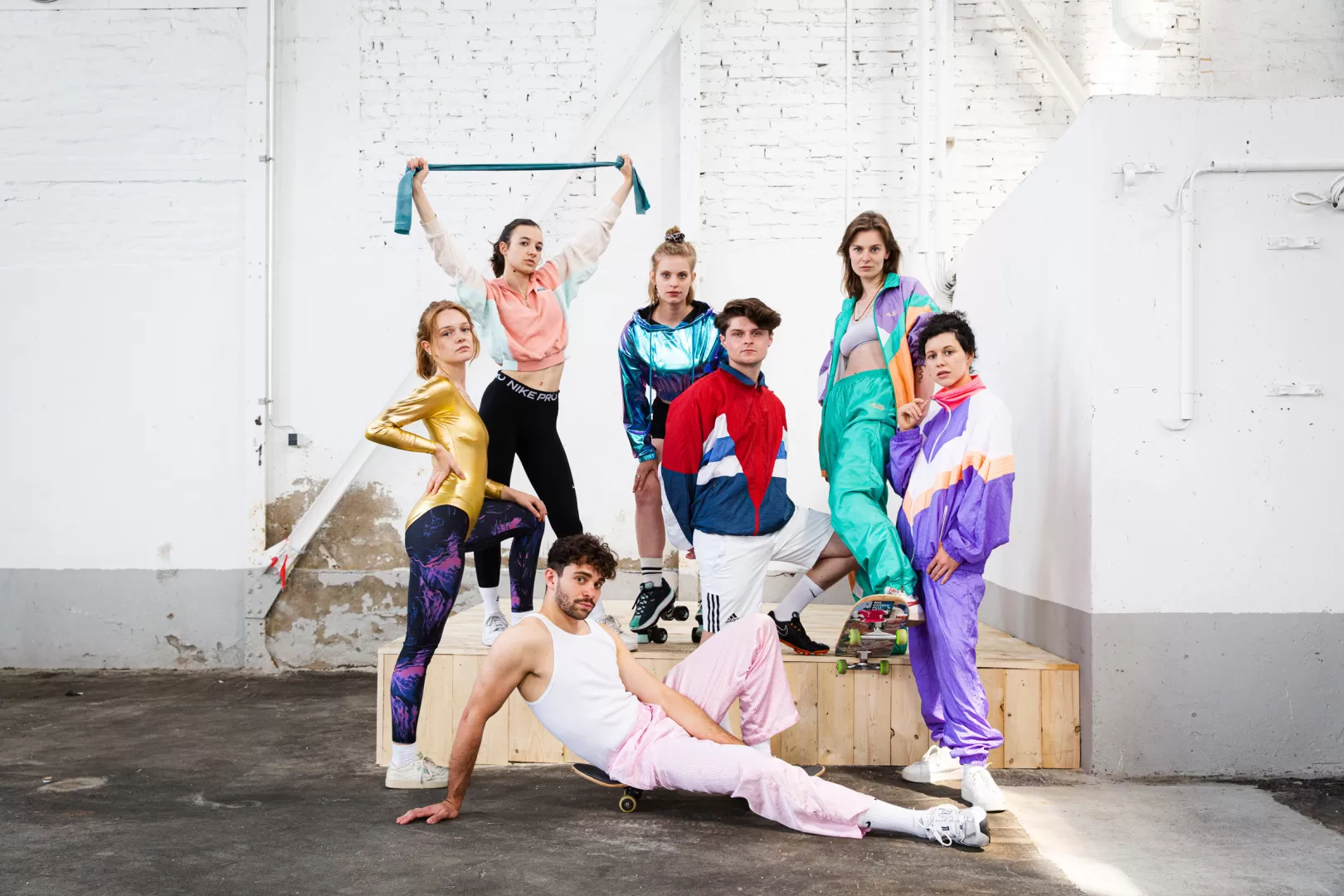 7 Studierende in bunten Traininganzügen in einer Lagerhalle.