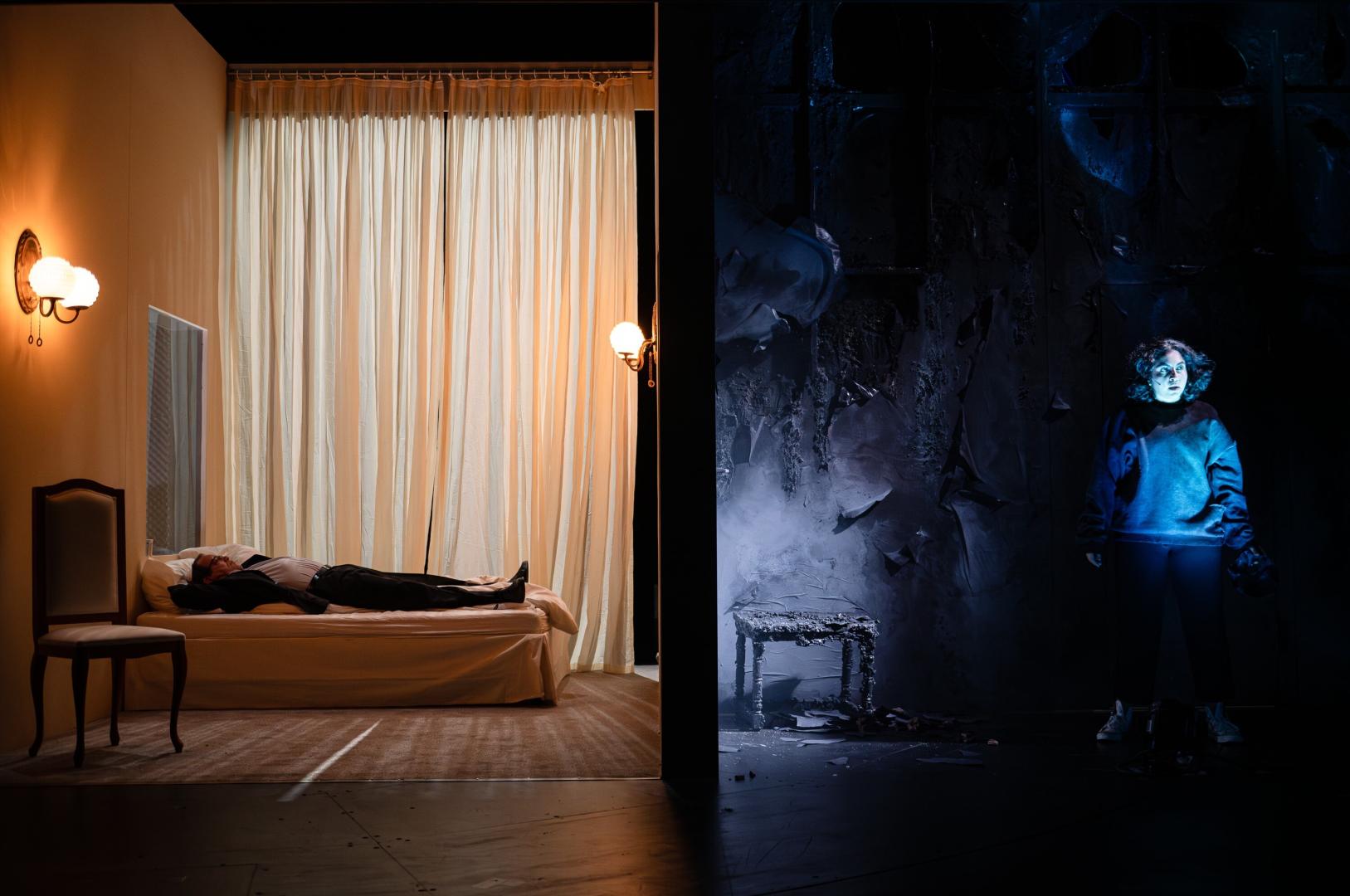 Zweigeteilter Bühnenraum. Links ein Hotelzimmer, rechts ein dunkler Raum.