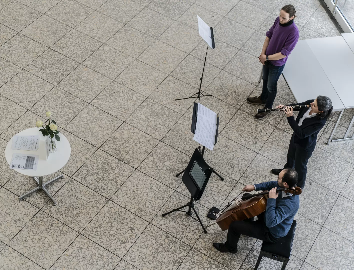 2 Musiker*innen und ein Sprecher während der Gedenkveranstaltung im Foyer der Hochschule, von oben betrachtet