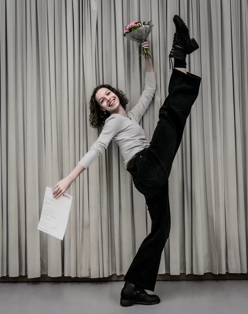 Julia Alsdorf, mit Urkunde und Blumen in den Händen, wirft ihr Bein hoch.