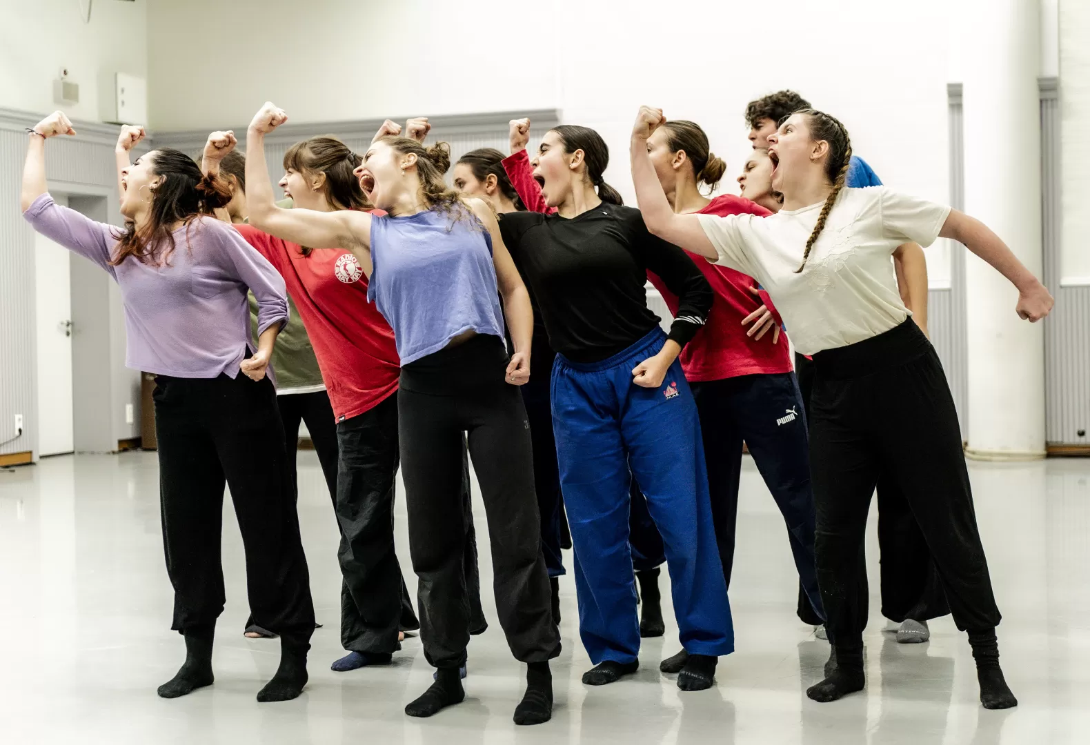Eine Gruppe Tänzerinnen. Alle schauen mit weit geöffnetem Mund und erhobener Faust nach rechts.