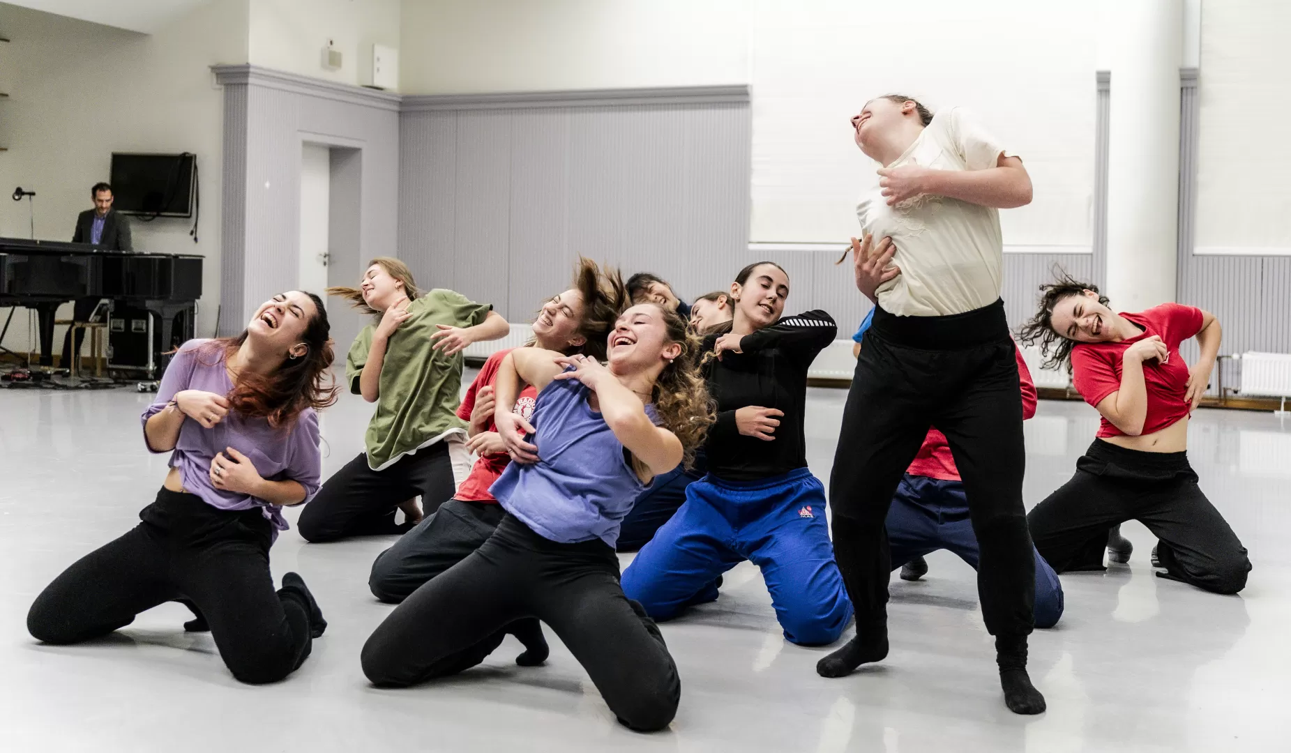Tänzerinnen knien lachend auf dem Boden und berühren ihren Oberkörper.