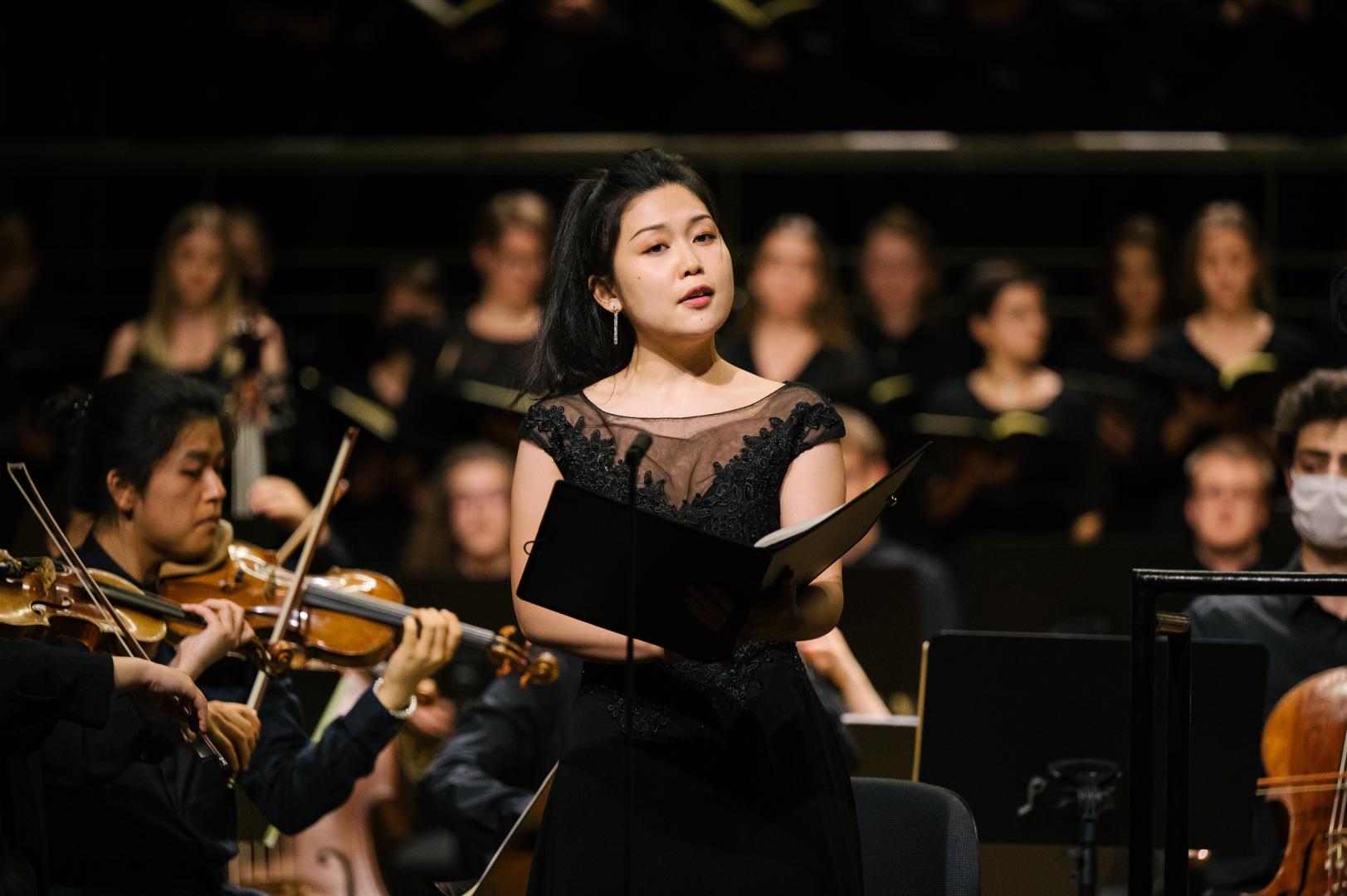 Solo-Sängerin in schwarzem Kleid mit dem HfMDK-Orchester auf der Bühne im Großen Saal
