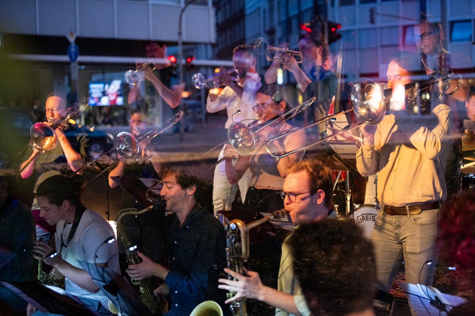 Bigband-Musiker*innen im Club ono2, durch das Fenster betrachtet