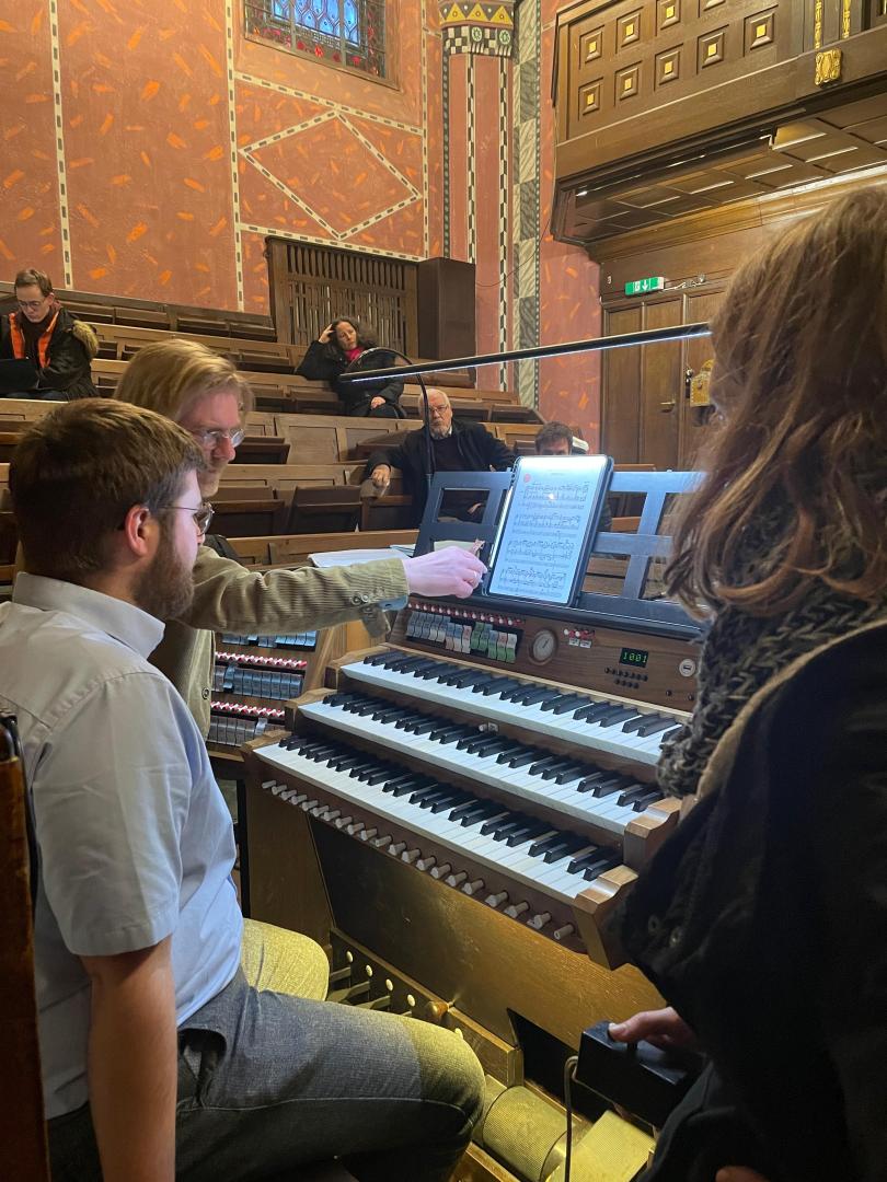 Prof. Carsten Wiebusch zeigt einem Studenten, der an der Orgel sitzt, eine besondere Stelle im Stück.