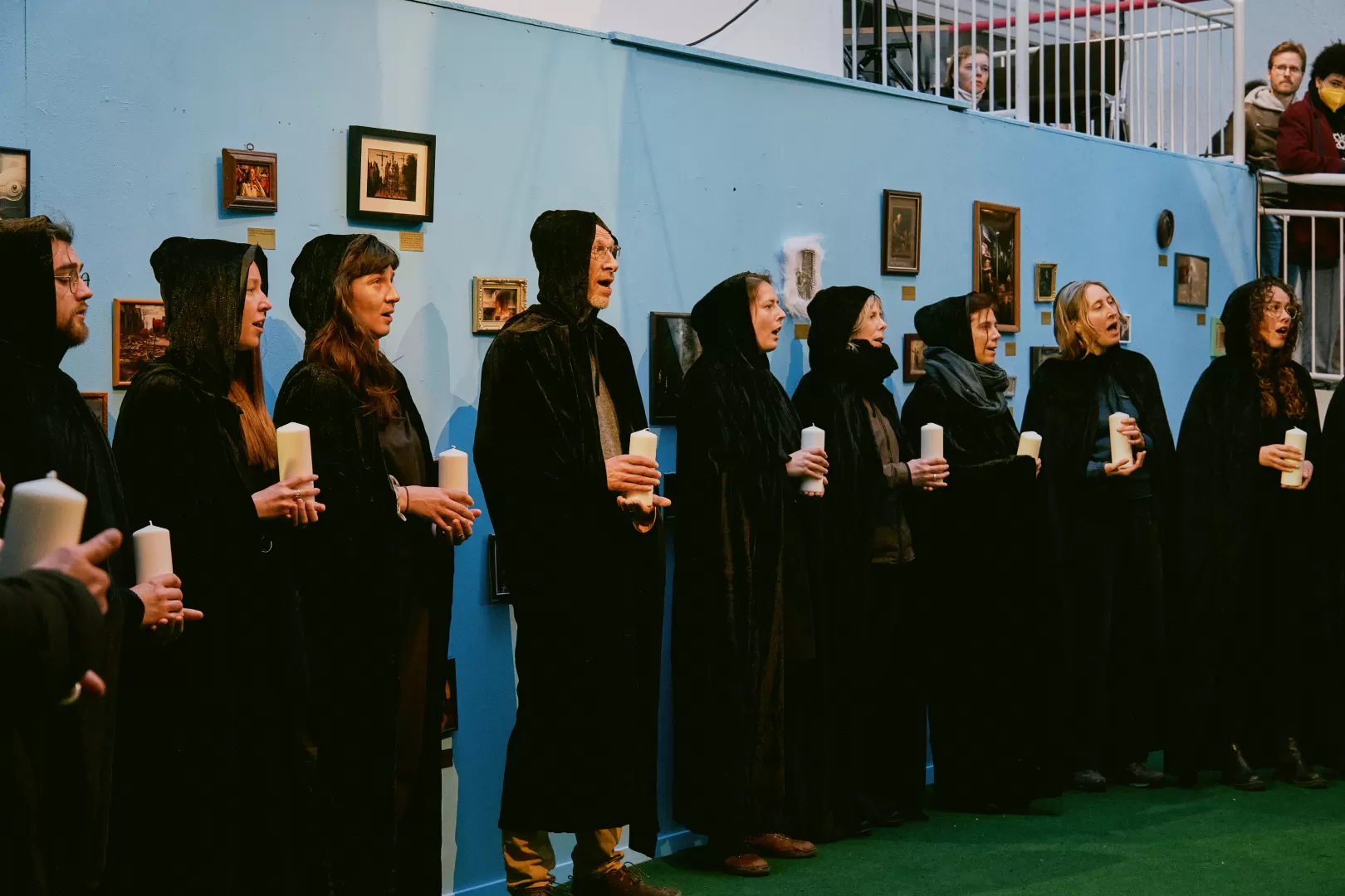 Personen in schwarzen Kutten singen mit Kerzen in der Hand.