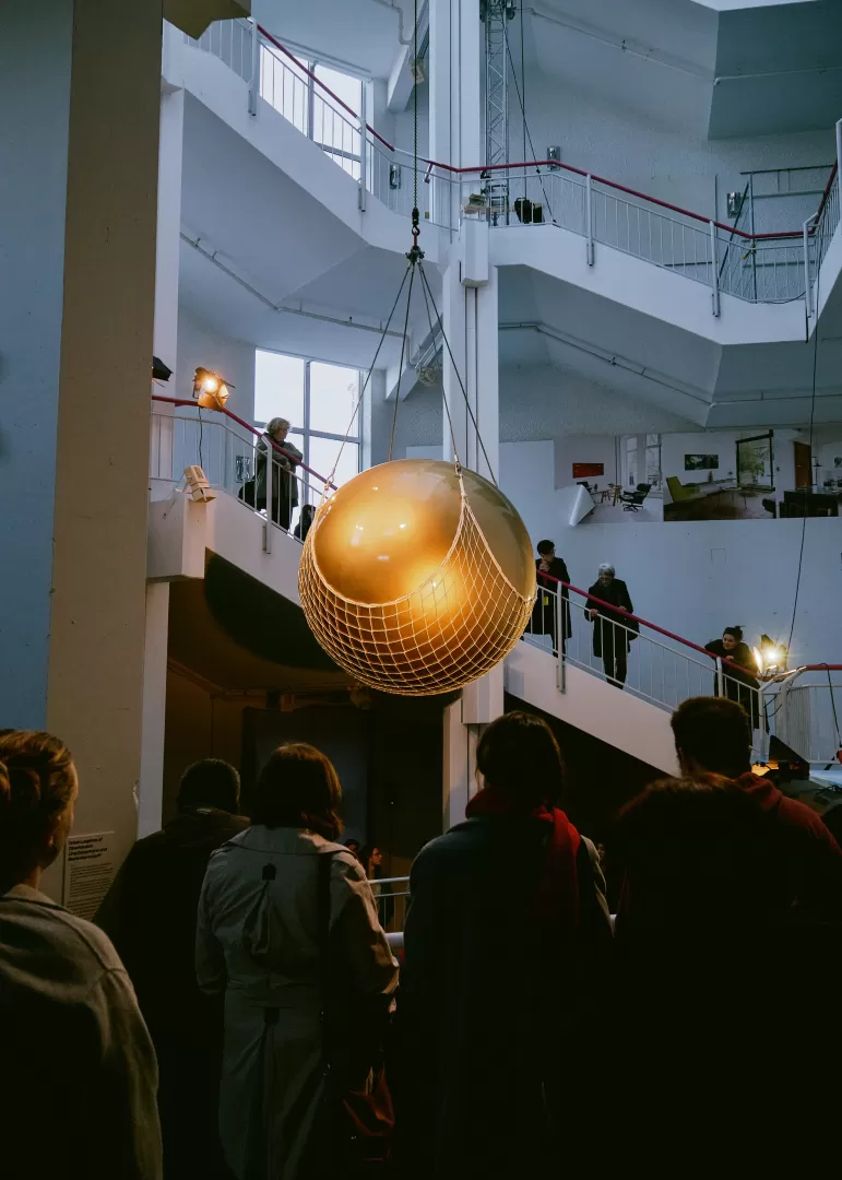 Die Goldene Kugel hängt über den in schwarzen Kutten gekleideten Mitwirkenden in einem weißen Treppenhaus.