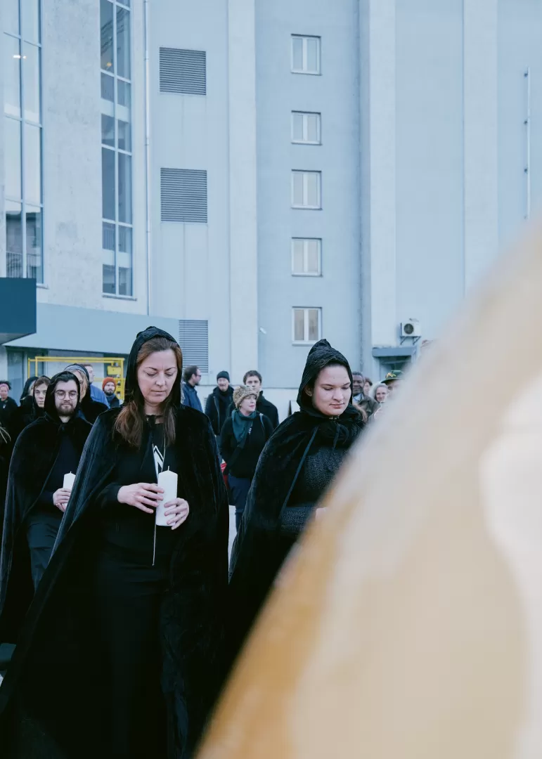 Die Personen in schwarzen Kutten stehen hinter der goldenen Kugel und blicken hinunter auf ihre Kerzen.