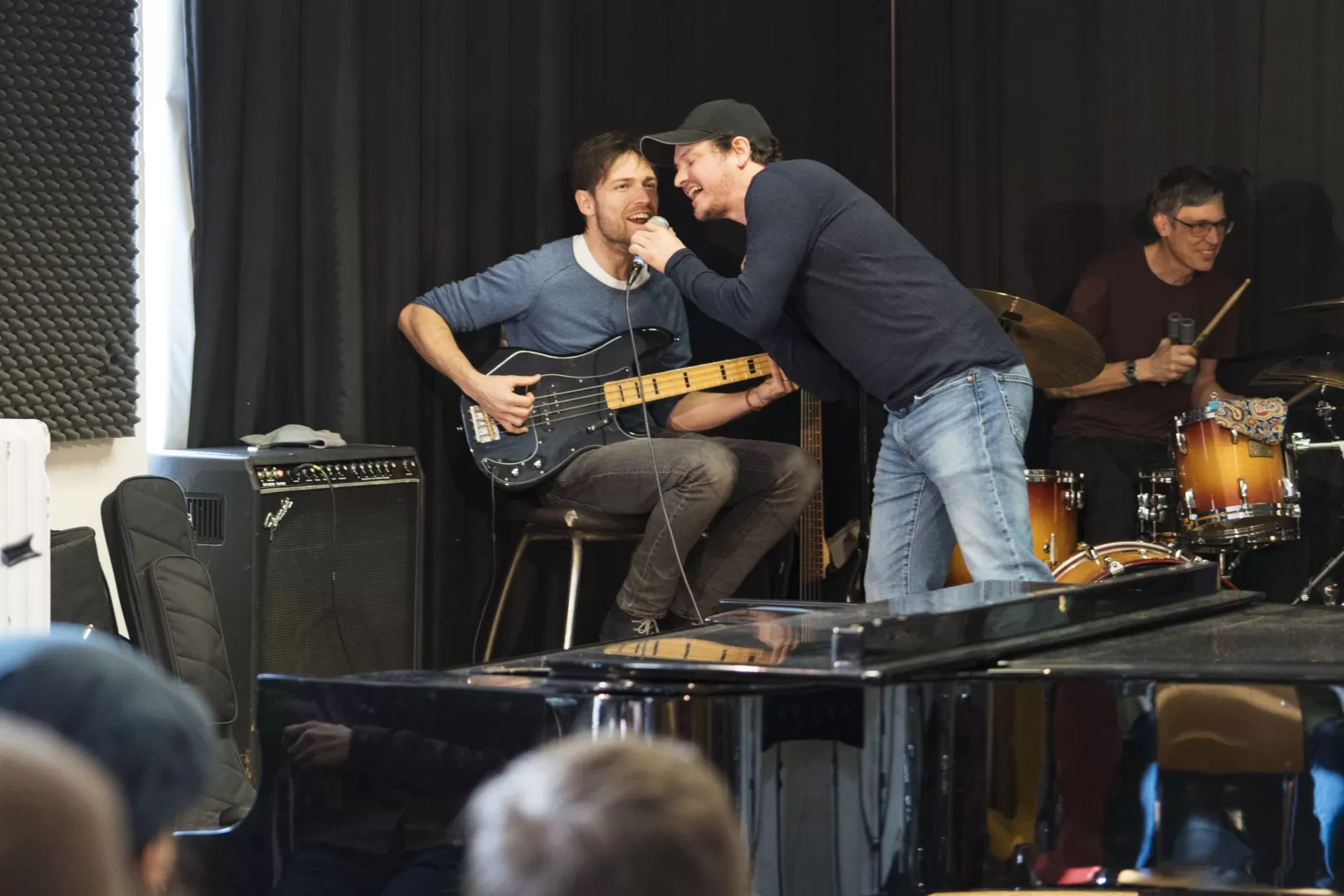 Ein interner Auftritt der Coach-Band. Zwei Coaches singen zusammen in ein Mikrofon. Einer von beiden sitzt auf einem Stuhl und spielt E-Bass.