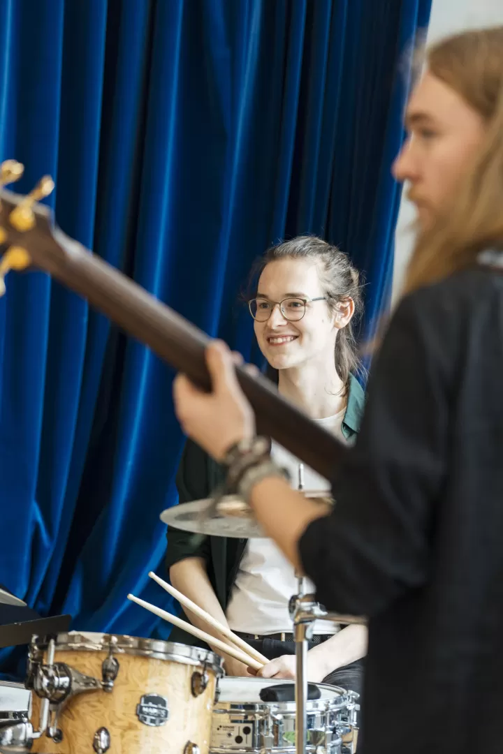 Ein lächelnder Schlagzeuger im Band-Coaching. Vorne rechts ist unscharf der Bassist zu sehen.