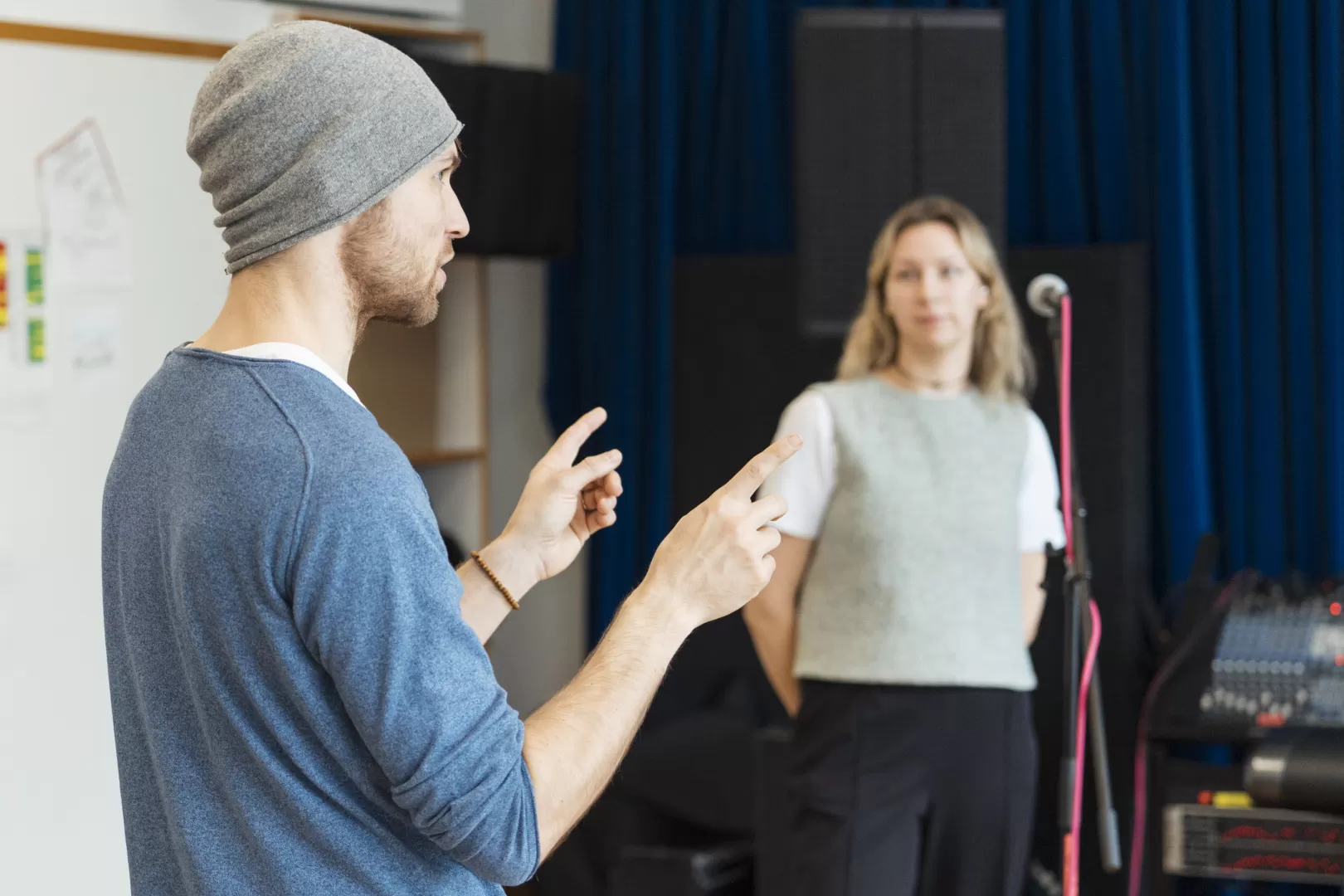 Der Coach Martin Bosch erklärt etwas und gestikuliert dabei mit seinen Armen. Im Hintergrund steht die Sängerin von Groovedivision und hört konzentriert zu.
