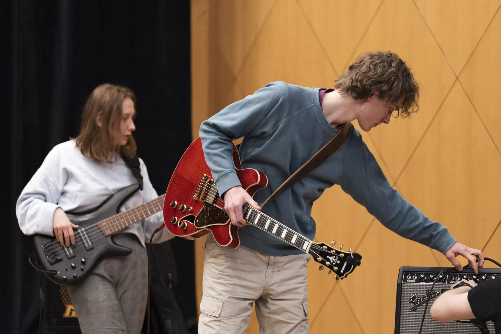 Ein Gitarrist verstellt etwas an einer Box. Links dahinter spielt die Bassistin.