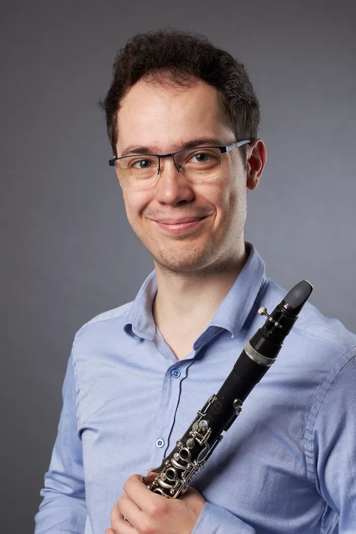 Bálint Gyimesi hält seine Klarinette in der Hand und lächelt in die Kamera.