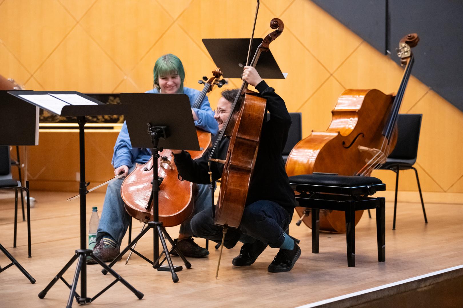 Eine Cellistin und ein Cellist lachen gemeinsam während einer Probe im Kleinen Saal