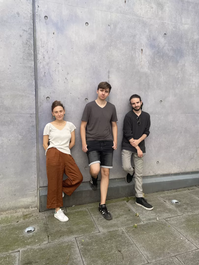 Die drei Musiker*innen des Sören Riesner Trios lehnen an einer grauen Betonwand.